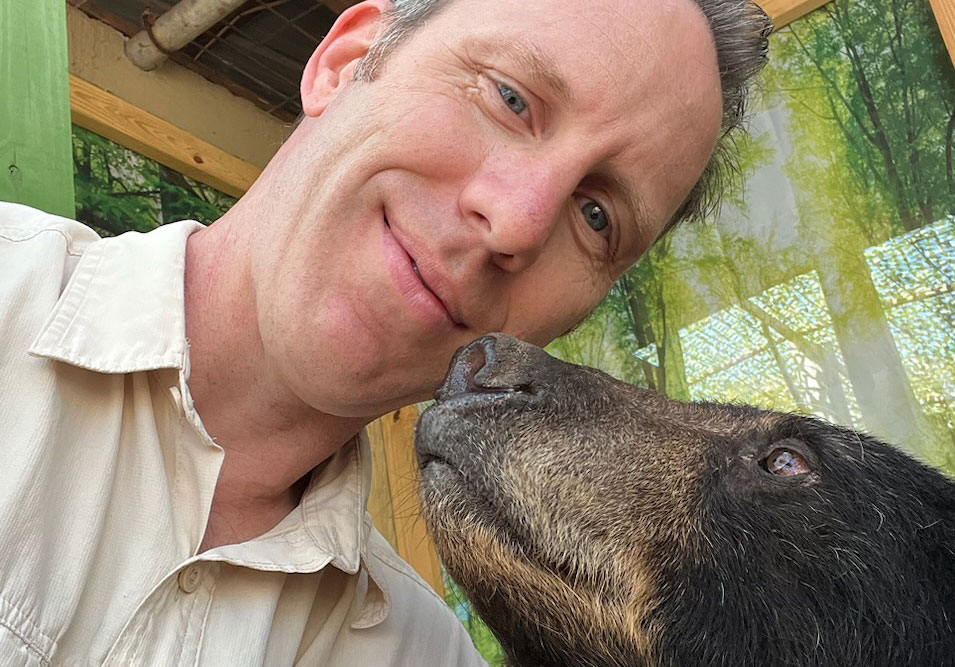man with his face next to a black bear